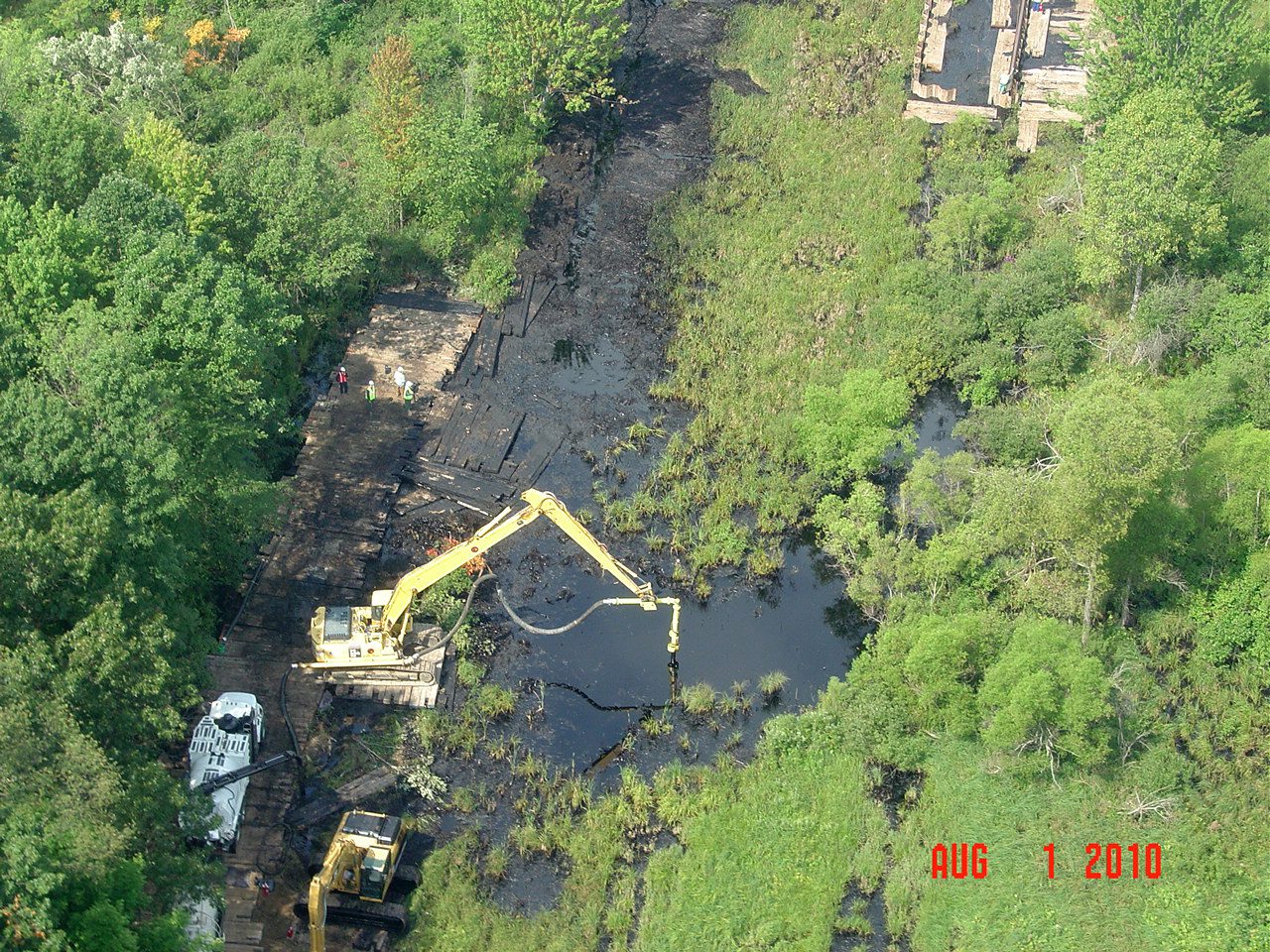 Aerial view of an excavator working an oil spill in a wooded creek.